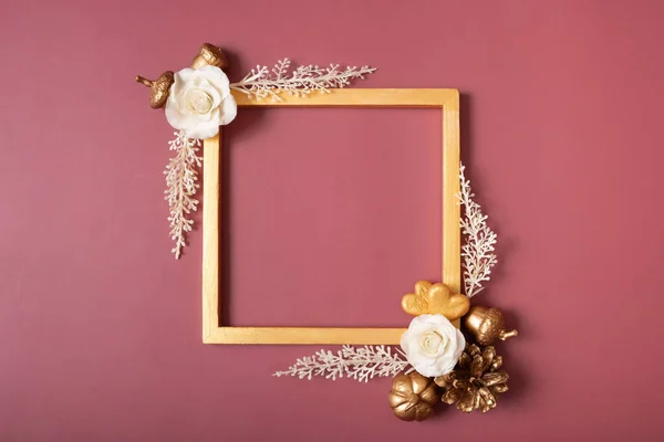 Square golden frame blank with flowers and golden hearts on red background. Flat lay, top view, copy space.