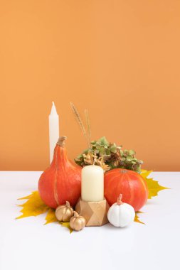 Sonbahar yaratıcı kompozisyonu. Beyaz turuncu arka planda kurumuş yaprak çelengi, balkabağı ve mum. Sonbahar ve Şükran Günü konsepti. Durgun hayat.