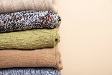 A stack of cozy knitted sweaters on beige background. Warm concept.