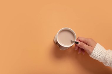 Female hand in sweater holding cup of cocoa on colored background, top view with copy space.