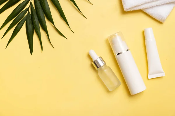 Cosmetic bottles for beauty massage therapy with towel. Flat lay on yellow background with palm leaves.