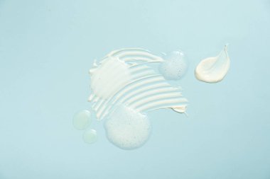 Various cosmetic smears on a blue background, top view. Lather soap foam, aloe vera clear transparent spot, facial moisturizer, body milk lotion and lipstick texture.