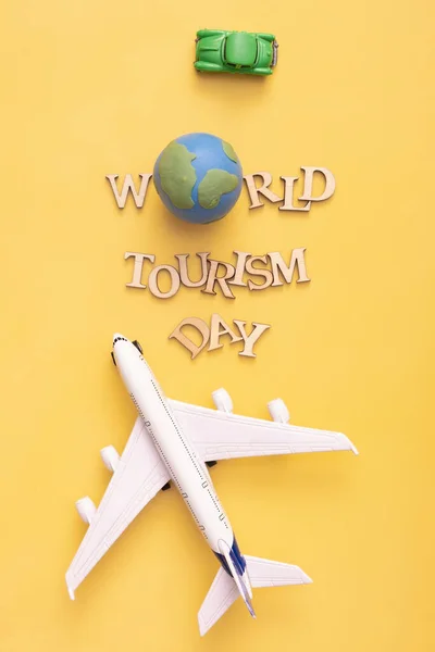 World Tourism Day text from wooden letters with globe, car and airplane on yellow background. Top view, flat lay.