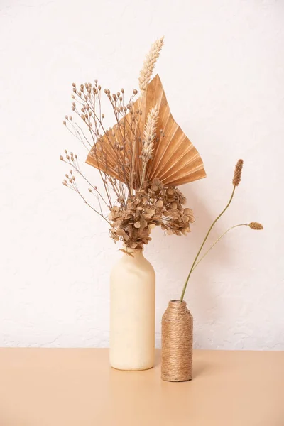 A bouquet of beige flowers and paper palm trees on white wall background.