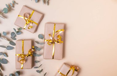Kraft kağıdına sarılı hediye kutuları altın kurdele ve pastel bej arka planda okaliptüs. Tatil hediyesi konsepti. Üst görünüm.
