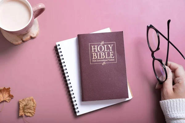 Holy Bible and female hand in sweater with glasses and a Cup of Coffee top view. Holy Bible study online concept.