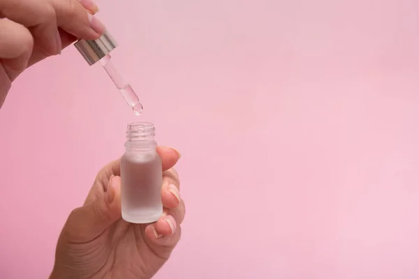 Cosmetic oil in dropper bottle in female hands. SPA and beauty therapy. Pink background with copy space