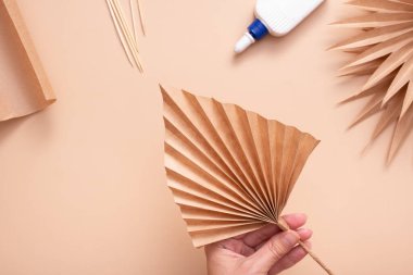 Dried palm leaf from paper in female hand top view. Creative handwork to create tropical leaves. Master class
