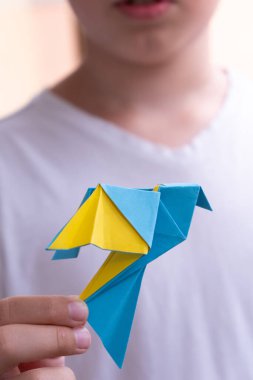 The boy holds a paper yellow-blue dove in his hands. Peace day symbol, prayer for peace in Ukraine concept