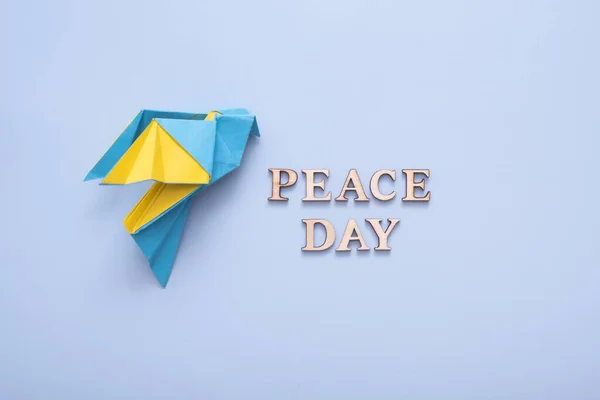 Peace day text from wooden letters with yellow-blue paper dove on blue background top view. International Peace day concept.