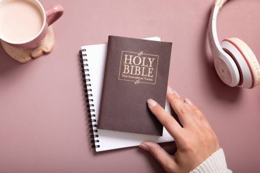 Holy Bible and female hand in sweater with a Cup of Coffee and headphones top view. Holy Bible study online concept.