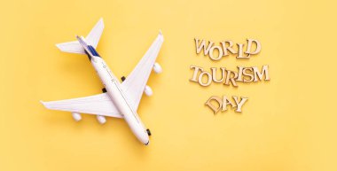 World Tourism Day text from wooden letters on a yellow background with airplane top view, flat lay.