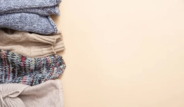 Stack of cozy knitted sweaters on beige background. Warm concept.