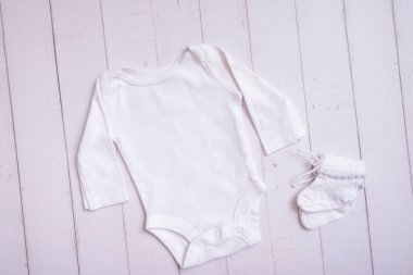 White baby bodysuit mockup for logo, text or design on wooden background top view.