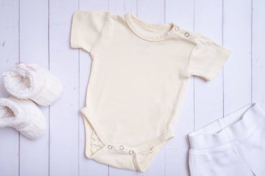 Yellow baby bodysuit mockup for logo, text or design on wooden background top view