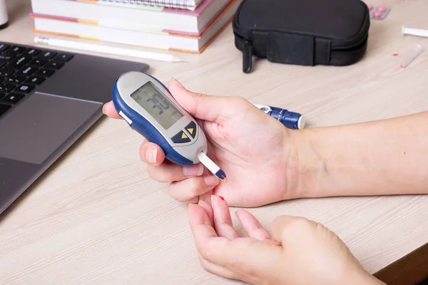 Female hands with a glucometer at the desk. The lifestyle of a person with diabetes, measuring the level of glucose in the blood.