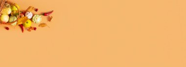 Autumn banner with harvest basket with corn, apples, zucchini and peppers on a orange background with copy space.