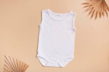 White baby bodysuit mock-up for logo, text or design on beige background with palm leaves top view