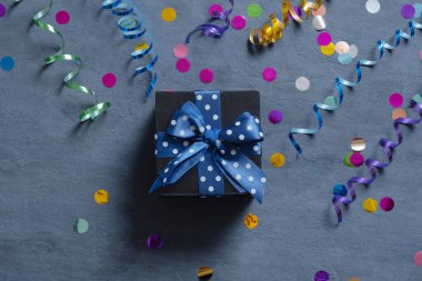 Siyah hediye kutusunda koyu çimento arka planında yay ve tatil süslemeleri vardı. Üst görünüm.