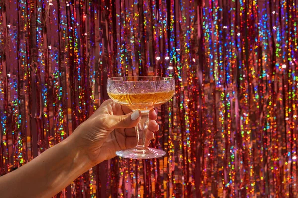 A glass of champagne in a woman\'s hand on the background of a festive New Year\'s party background.