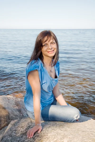 Beautiful woman sitting on a rock by the lake — Stock Photo, Image