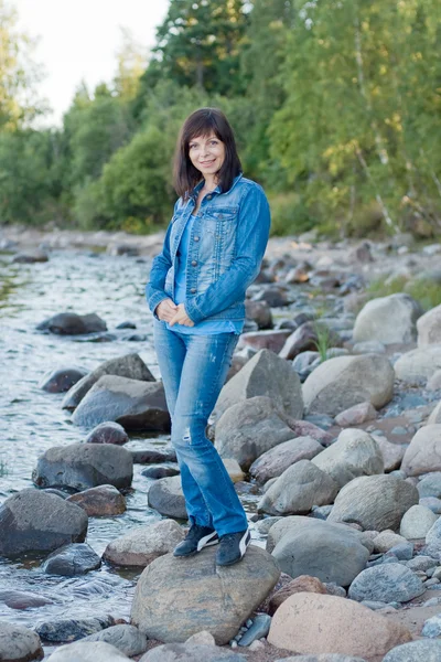 Mulher bonita está de pé sobre uma rocha junto ao lago — Fotografia de Stock