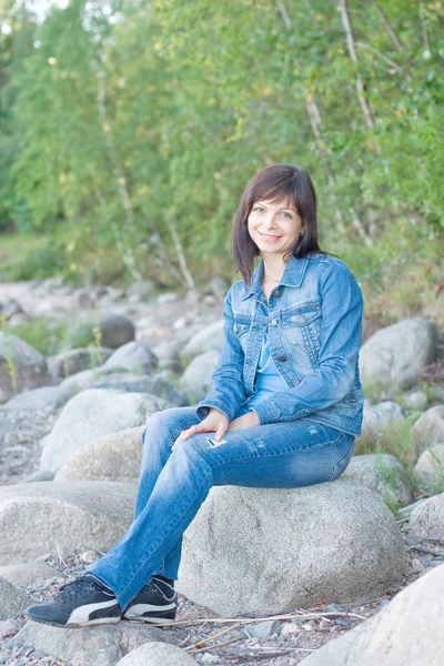 Pretty woman sitting on a rock by the lake — Stock Photo, Image