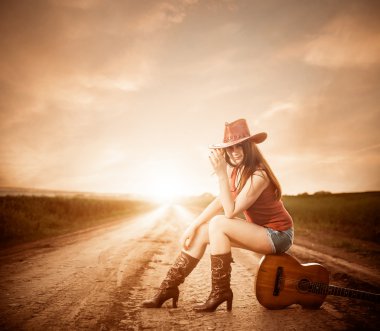 Stylish cowgirl on a sunset road clipart