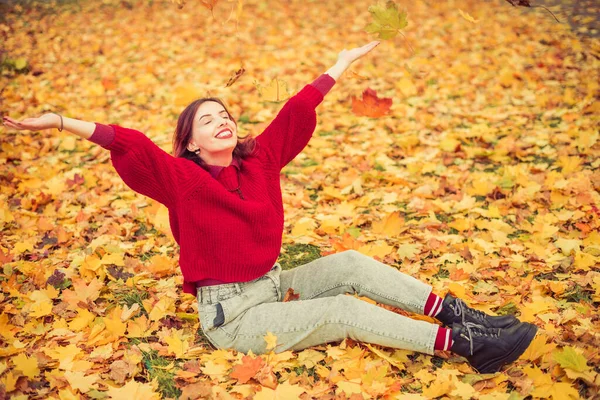 穿着红毛衣的年轻快乐的女人 坐在五彩缤纷的秋叶里 — 图库照片