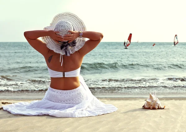 Mulher de chapéu senta-se na praia . — Fotografia de Stock