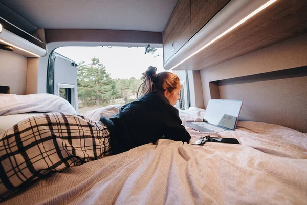パジャマの若い女性のデジタルノマドは Rvの旅行中にリモートで働いている間 ベッドに横たわってネット上のデータを閲覧しています ロイヤリティフリーのストック写真
