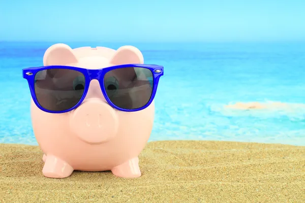 Summer piggy bank with sunglasses on the beach — Stock Photo, Image