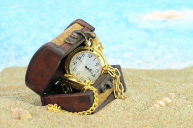 Antique pocket clock in a treasure chest on a beach clipart