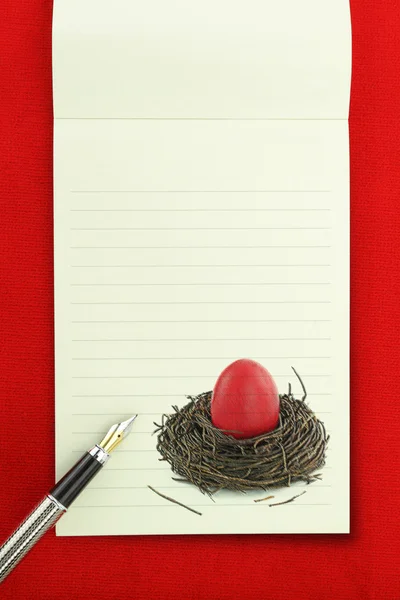 Cuaderno de Pascua, huevo de Pascua rojo en el nido en la página del cuaderno en blanco —  Fotos de Stock