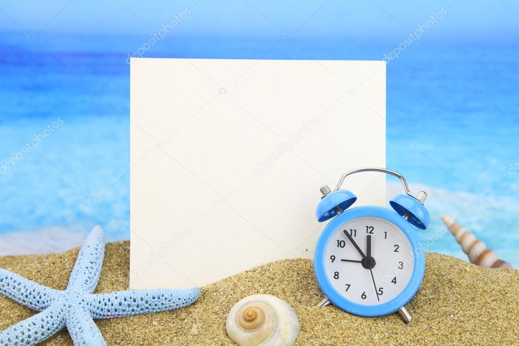 Summer time. Paper card and alarm clock on the beach