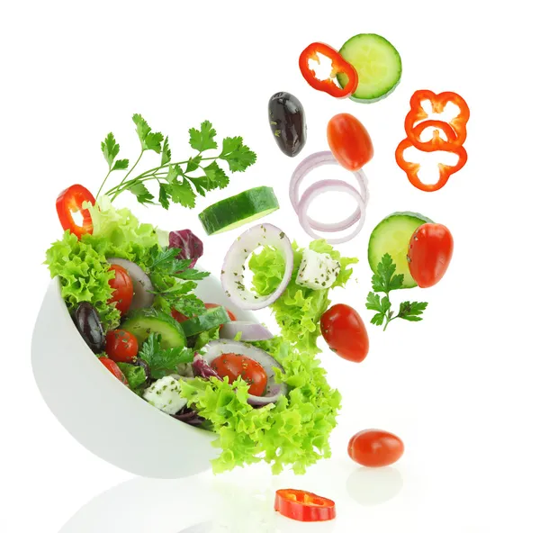 Légumes frais mélangés tombant dans un bol de salade Photo De Stock