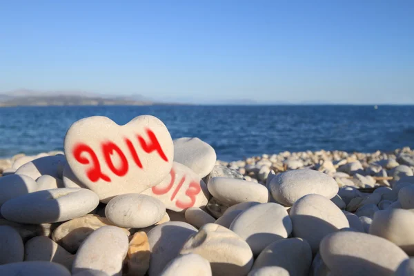 Nový rok 2014 na kámen ve tvaru srdce na pláži s stopa spreje — Stock fotografie