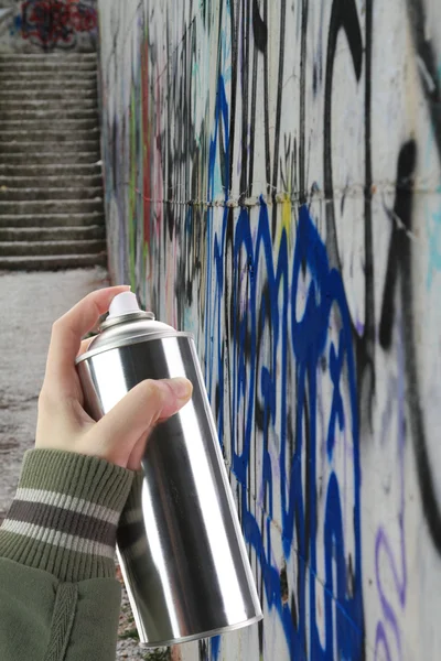 Человеческая рука держит банку с граффити-спреем перед красочной стеной — стоковое фото