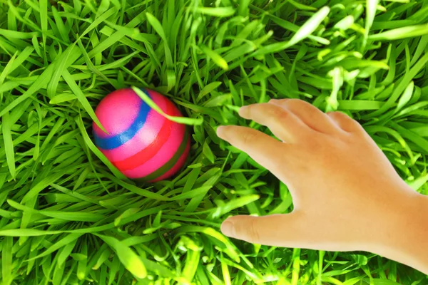 Рука тянется за пасхальным яйцом на зеленой траве — стоковое фото