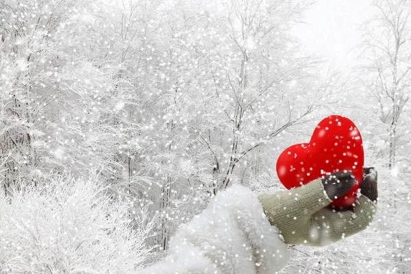 Mulher mão segurando um coração vermelho em um fundo nevado — Fotografia de Stock