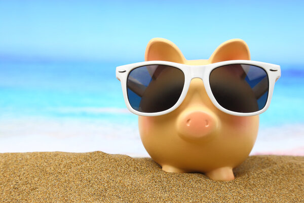 Summer piggy bank with sunglasses on the beach