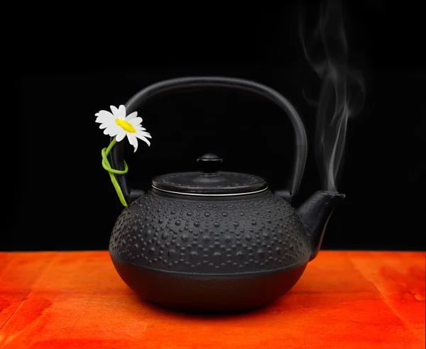 Teapot with chamomile flower and smoke on tabletop Stock Picture