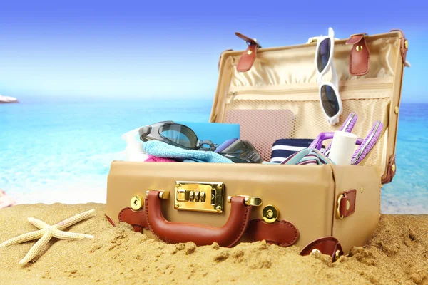 Full open suitcase on tropical beach background — Stock Photo, Image