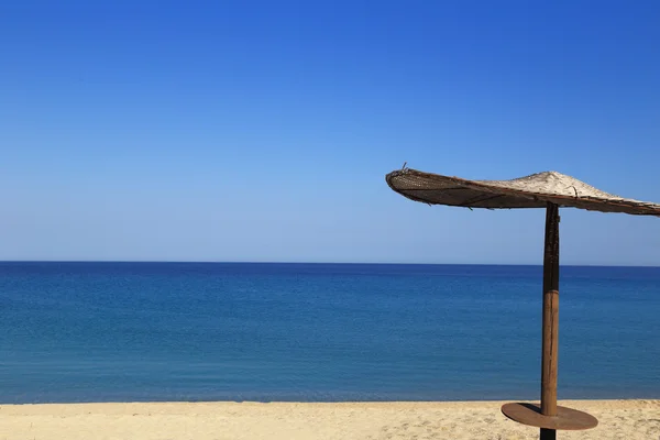 Солнечный пляж с плетеным зонтиком — стоковое фото