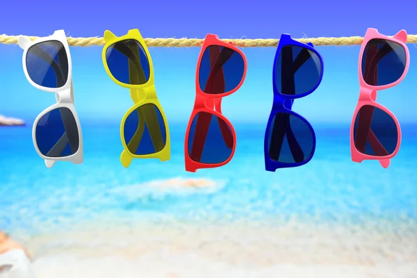 Coloridas gafas de sol colgadas en una cuerda frente al mar —  Fotos de Stock