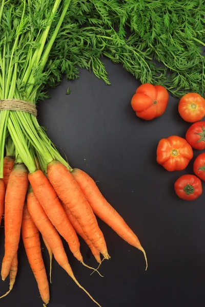 Verse wortelen met bladeren en tomaten op blackboard — Stockfoto