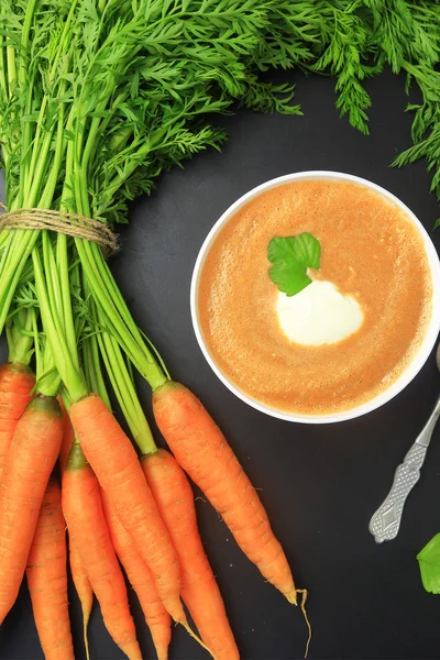 Zanahorias frescas con hojas y sopa en pizarra —  Fotos de Stock