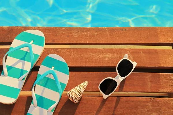 Flip flops and sunglasses on wooden planks and water — Stock Photo, Image