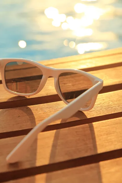 Солнечные очки на деревянных досках и вода на закате — стоковое фото