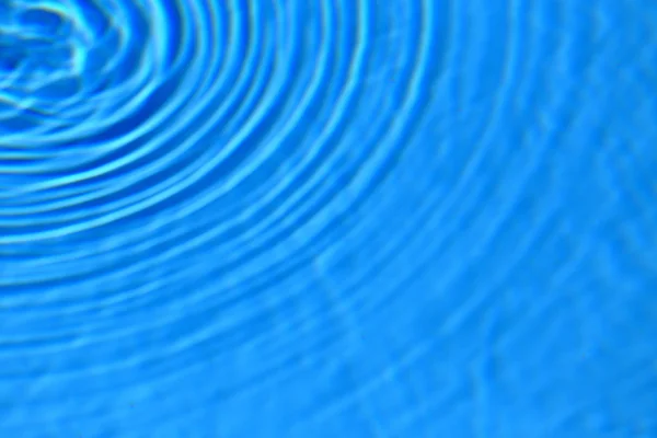 Sininen kirkas vesi pyöreä aaltoilu puolella tausta — kuvapankkivalokuva